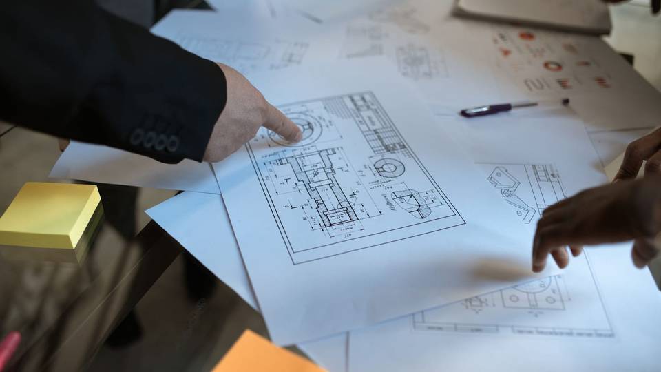 أيدٍ تشير إلى مخططات هندسية مطبوعة على طاولة اجتماع