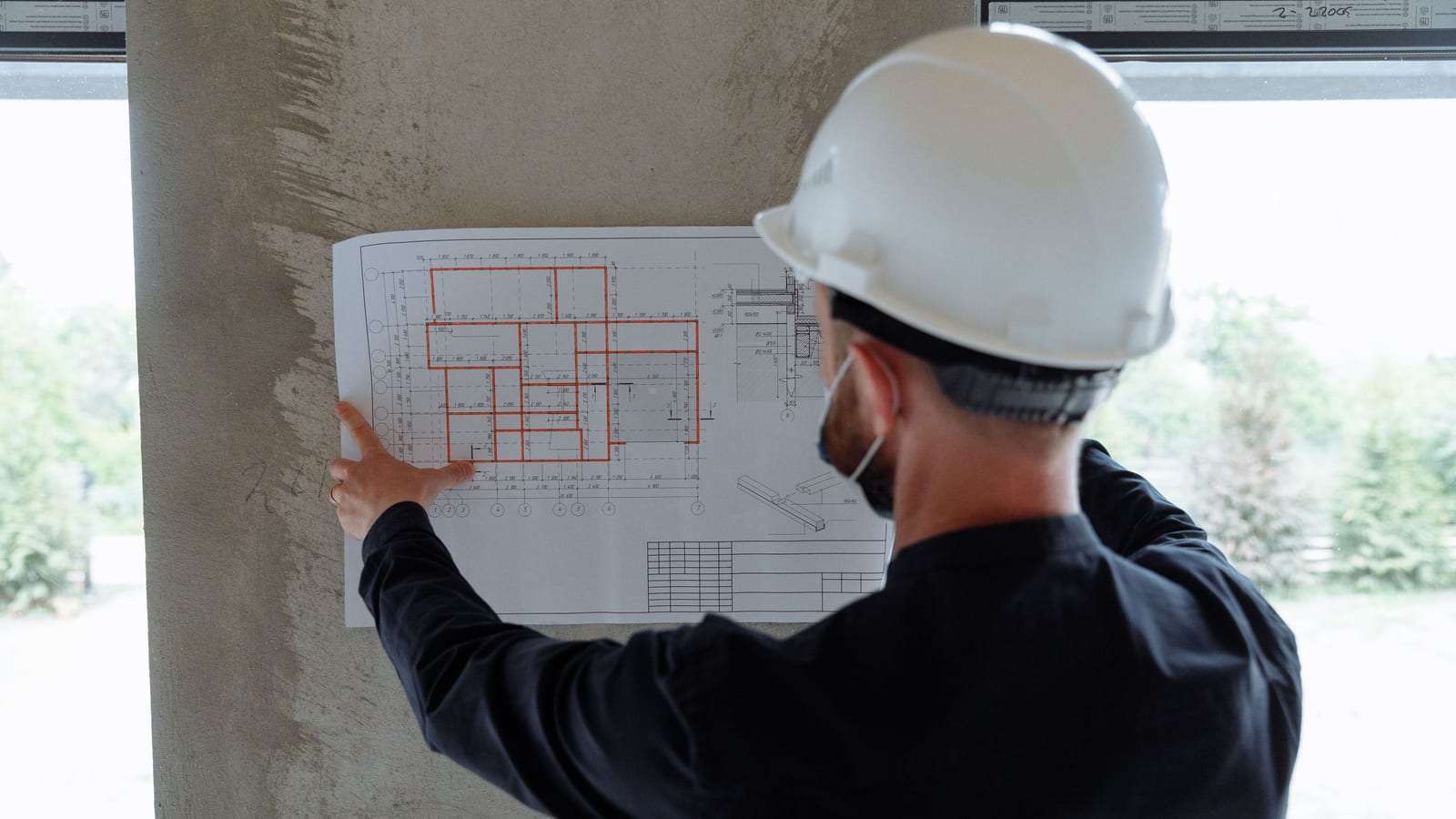 مهندس بخوذة بيضاء يثبت مخططاً على عمود خرساني ويراجعه في الموقع
