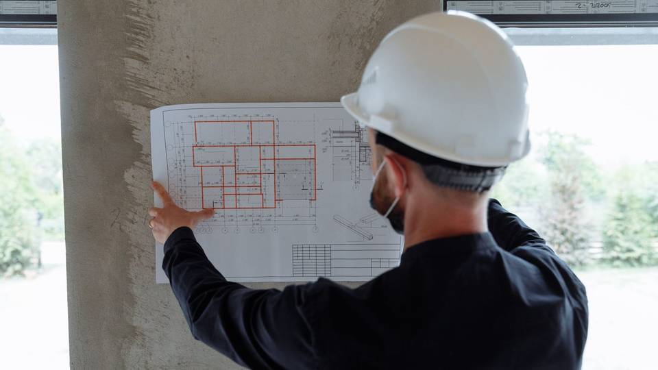 مهندس بخوذة بيضاء يثبت مخططاً على عمود خرساني ويراجعه في الموقع