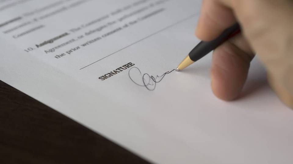 يد توقع بقلم على خانة التوقيع في عقد مطبوع