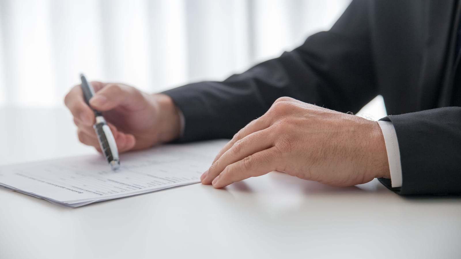 شخص ببدلة داكنة يملأ مستنداً على مكتب أبيض