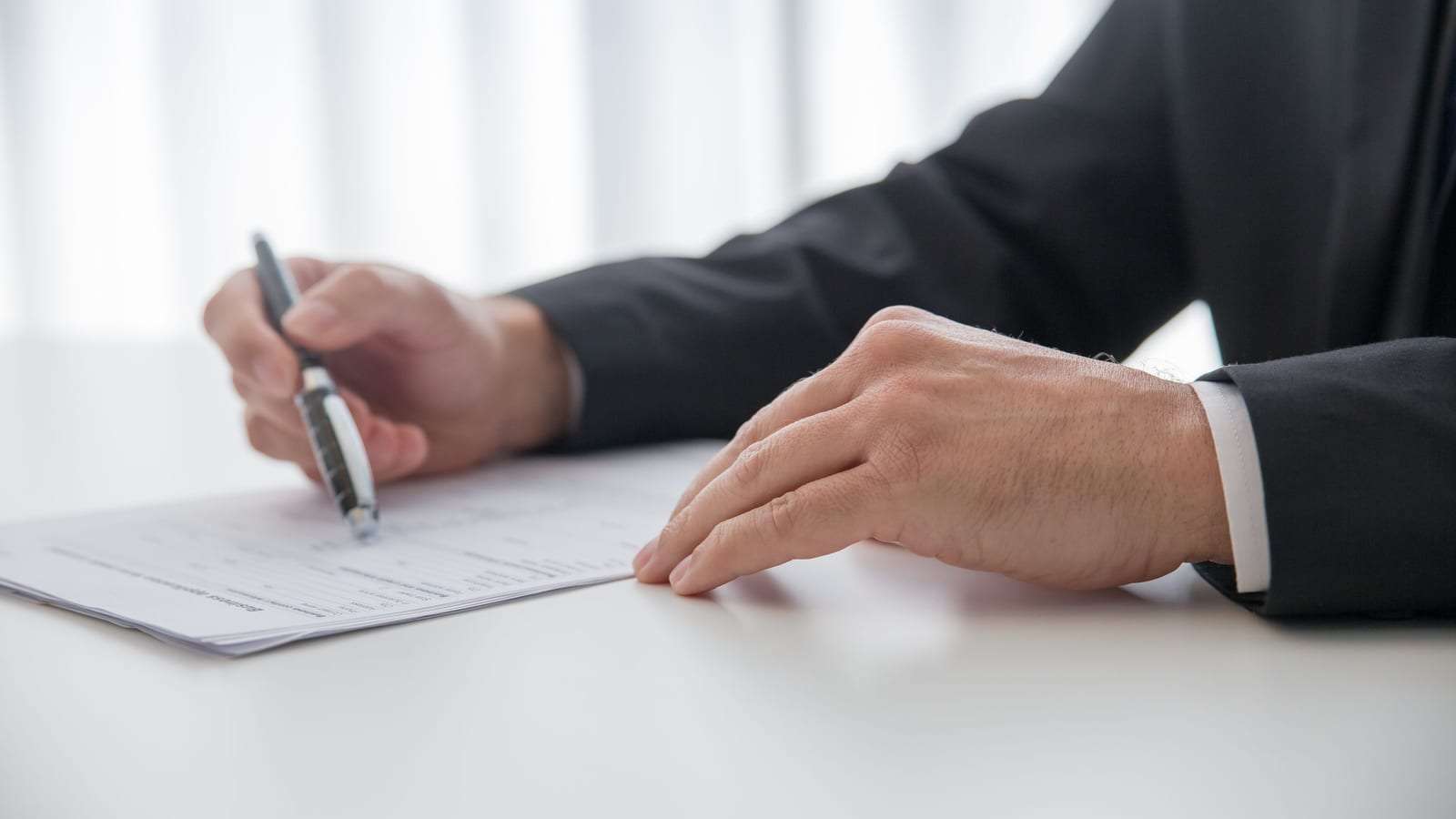 شخص ببدلة داكنة يملأ مستنداً على مكتب أبيض